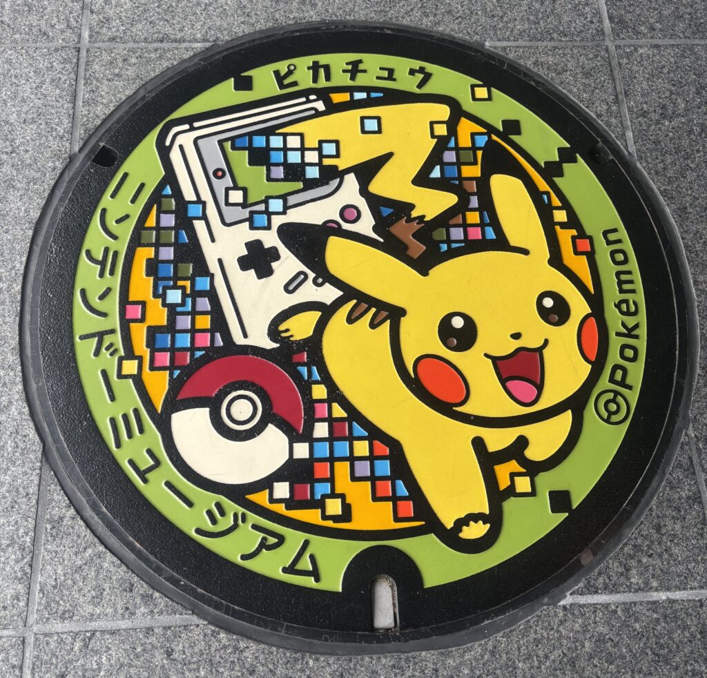 ニンテンドーミュージアムの屋外にある、ゲームボーイとピカチュウとモンスターボールが描かれたカラフルなマンホール